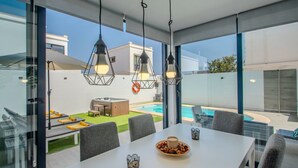 Un comedor moderno con una mesa blanca, sillas grises y lámparas colgantes.