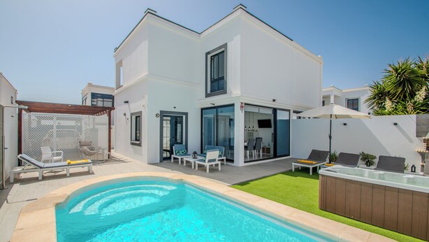 Una casa moderna de dos pisos con piscina, mobiliario exterior y zona de patio.