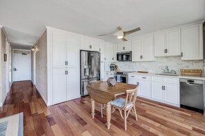 A kitchen with white cabinets, a wooden dining table, and a ceiling fan. - Maui Parkshore #415 Ocean View in the Heart of Kihei, Walk to Kamaole Beach (Kihei)