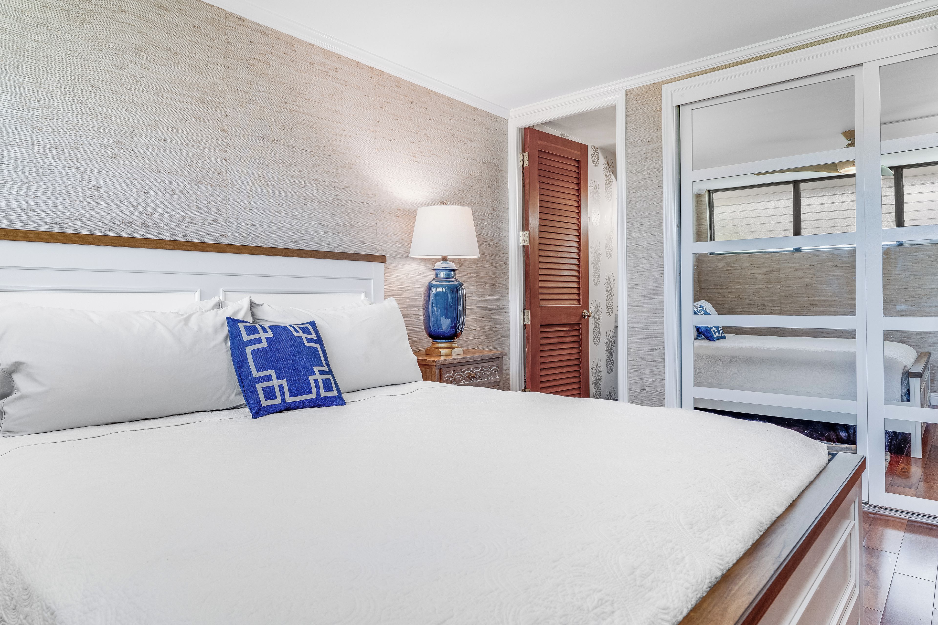 A hotel room with a large bed, a nightstand with a lamp, a wooden door, and a view of a balcony.