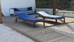 Een houten terras met twee ligbedden en een bank.
