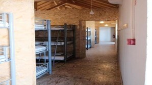 Een kamer met zichtbare houten balken, metalen stapelbedden en een gang naar een andere kamer.