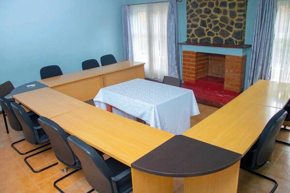 Uma sala de conferência com uma mesa comprida, cadeiras, uma pequena mesa com toalha branca e uma lareira de pedra.