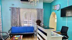 A reception desk, a blue sofa, a small table with magazines, a black office chair, and a chandelier.