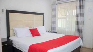 A hotel room with a large bed, a nightstand, a bedside table, and a window with curtains.