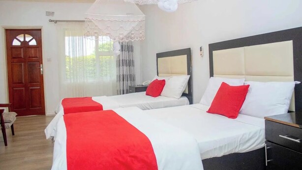 A hotel room with two beds, a wooden door, a window with curtains, and a bedside table.