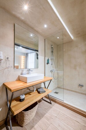 Een moderne badkamer met een grote spiegel, een houten wastafelmeubel, een douchecabine met glazen wanden en een lamp aan het plafond.