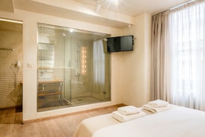 A hotel room with a large window, a shower area, a bed with towels, and a mounted TV. - Panellinion Beachfront Getaway - Triple Sea Gem (Kalamata)
