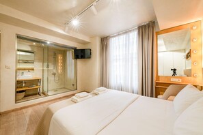 A hotel room with a large bed, a glass-enclosed shower, a vanity with a mirror, and a television. - Panellinion Beachfront Getaway - Triple Sea Gem (Kalamata)