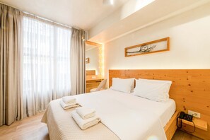 A hotel room with a wooden headboard, a bed with white linens, a bedside table with a phone, and a mirror with lights. - Panellinion Beachfront Getaway - Triple Sea Gem (Kalamata)