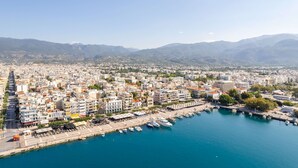 Un paisaje urbano costero con un puerto deportivo, edificios y montañas al fondo.