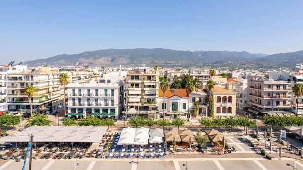Un paisaje urbano costero con edificios de varios pisos, cielo despejado y montañas a la distancia.
