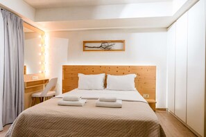 Ein Hotelzimmer mit einem hölzernen Kopfteil, einem Bett mit weißer Bettwäsche, einem Schreibtisch mit Stuhl, einem beleuchteten Spiegel und einem gerahmten Bild an der Wand.