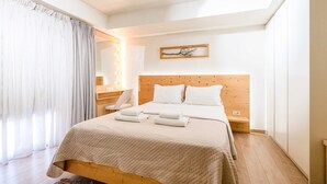 A bedroom with a wooden bed, white bedding, a bedside table, a mirror, and a lighted wall. - Panellinion Beachfront Gem Comfy Cozy Triple (Kalamata)