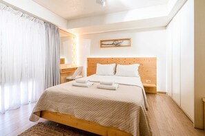A bedroom with a wooden bed, white bedding, a bedside table, a mirror, and a lighted wall. - Panellinion Beachfront Gem Comfy Cozy Triple (Kalamata)