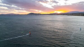 A wide body of water with a sunset in the background, a distant shoreline, and a few people on the water. - Panellinion Beachfront Gem Comfy Cozy Triple (Kalamata)