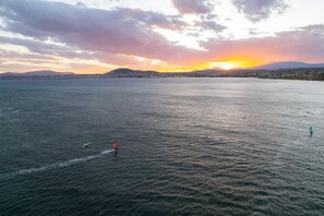 A wide body of water with a sunset in the background, a distant shoreline, and a few people on the water. - Panellinion Beachfront Gem Comfy Cozy Triple (Kalamata)