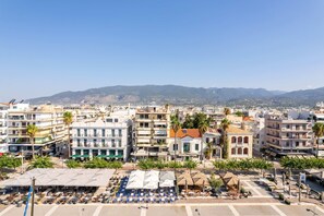 A coastal cityscape with multi-story buildings, a clear sky, and distant mountains. - Panellinion Beachfront Gem Comfy Cozy Triple (Kalamata)