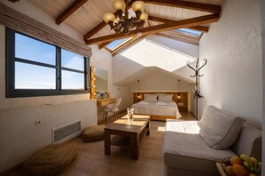 A high-ceilinged room with a sloped roof, a bed, a sofa, a table, and a mirror. - Panellinion Beachfront Suite With Private Jacuzzi (Kalamata)