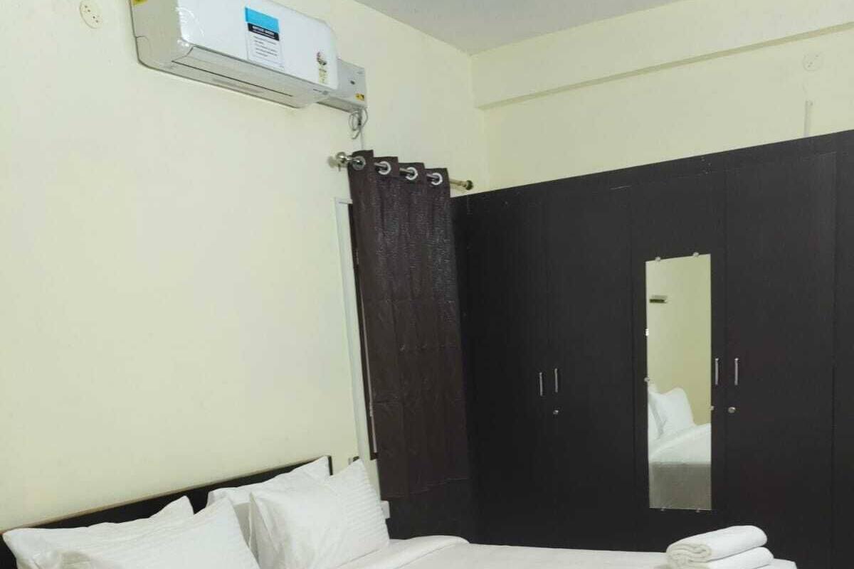 Una cama bien hecha con sábanas blancas, un armario de madera oscura, un espejo y un aire acondicionado instalado en la pared.