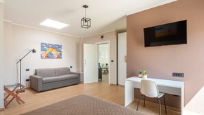 En moderne stue med en grå sofa, et hvidt skrivebord og et fjernsyn ophængt på væggen.