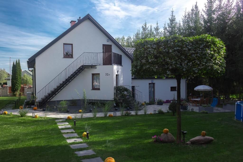 A two-story white house with a balcony, a staircase, and a well-maintained garden with pumpkins.