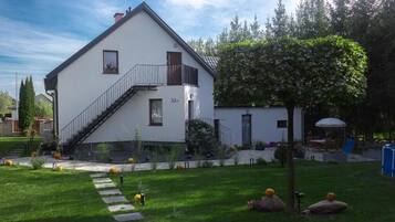 A two-story white house with a balcony, a staircase, and a well-maintained garden with pumpkins.
