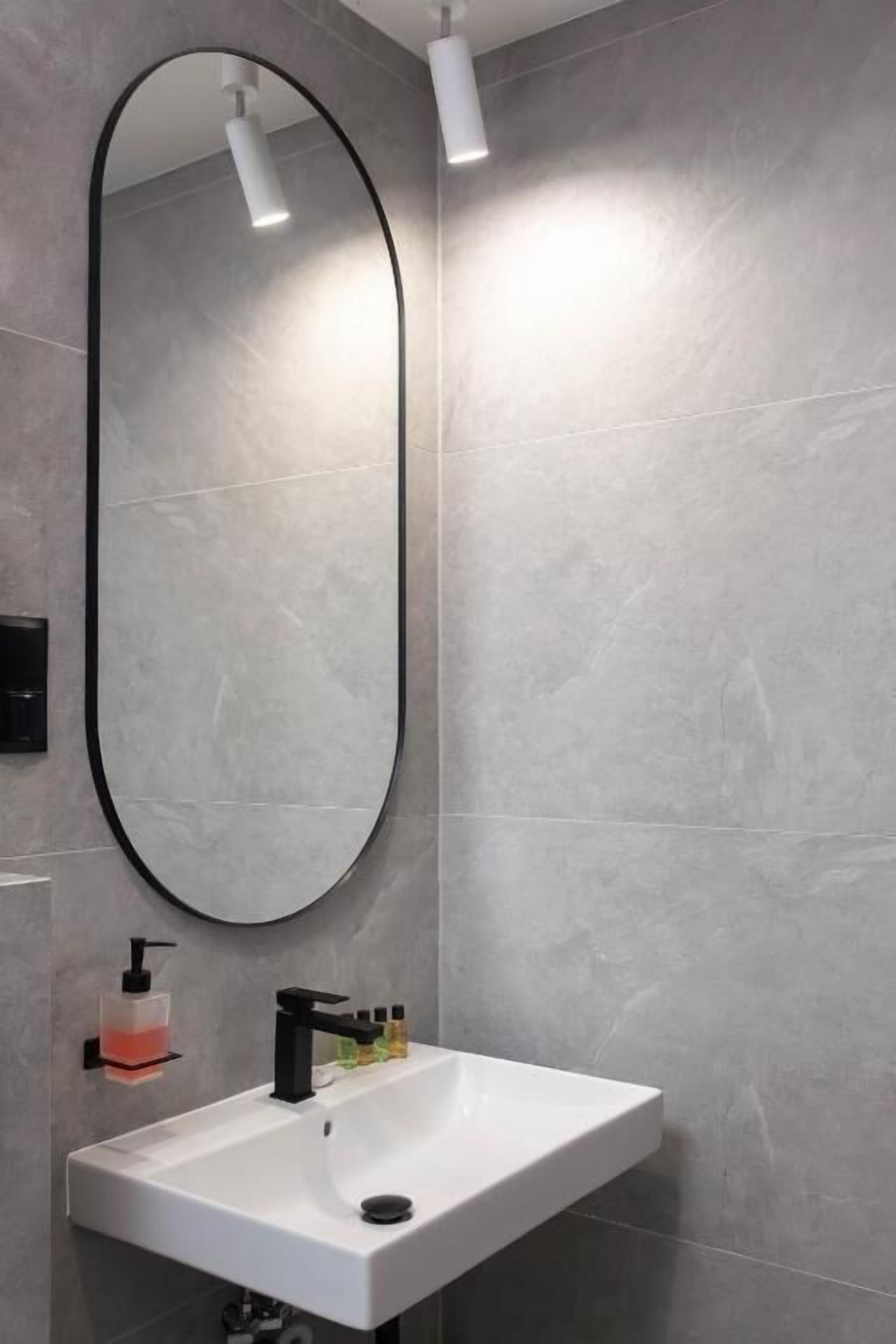 A bathroom with a white sink, black faucet, and a large oval mirror.