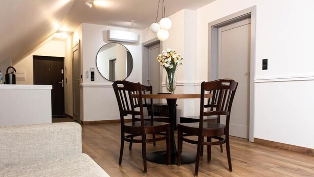 A dining area with a round table, four wooden chairs, a vase with flowers, and a mirror on the wall. - Lipowa32 Apartamenty (Hrubieszów)
