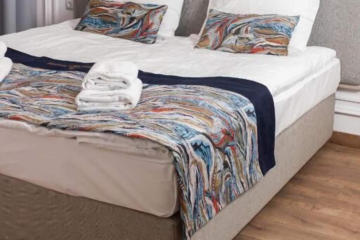 Ein Bett mit grauem Kopfteil, weißen Leinentüchern und farbenfrohen Kissen.