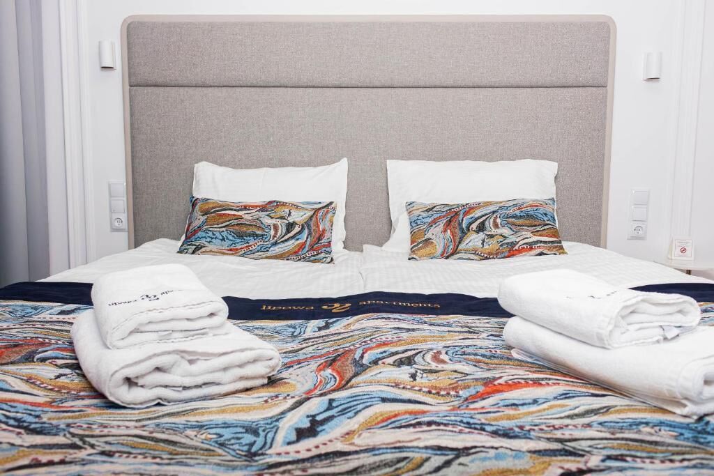 Una cama bien hecha con una colcha estampada, dos almohadas con un diseño colorido y dos toallas blancas dobladas.