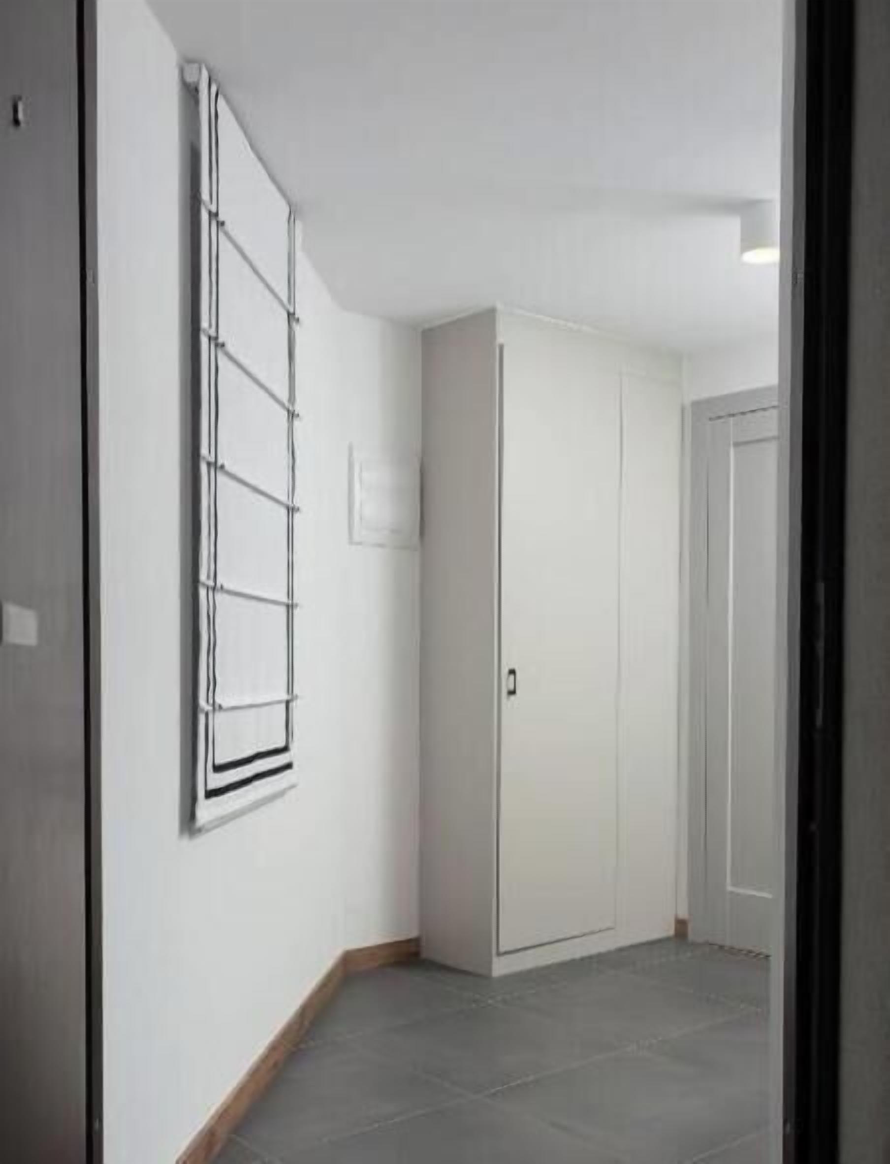 A hallway with a white wardrobe, a window with blinds, and a door.