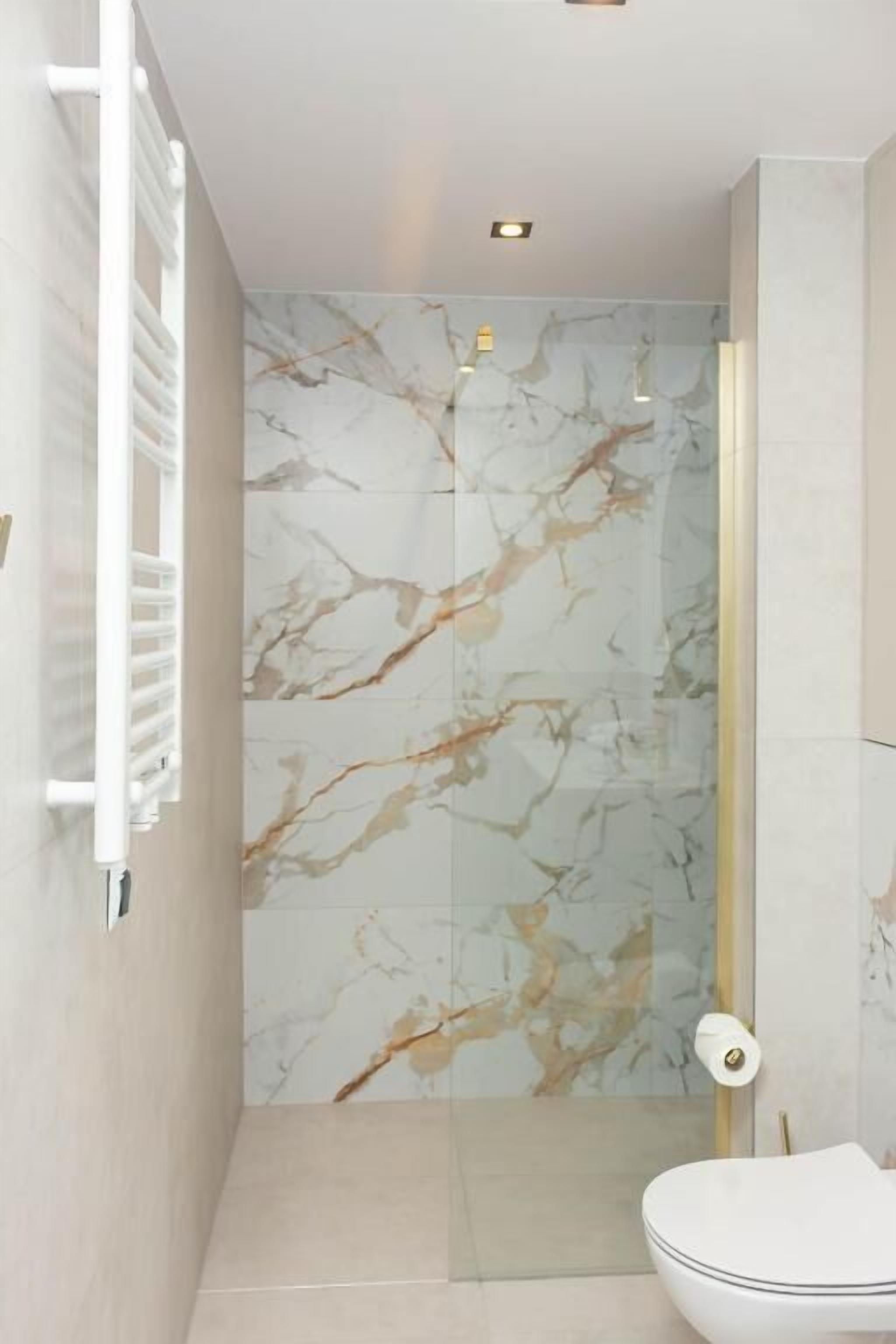 A modern bathroom with a marble shower wall, a toilet, and a towel rack.