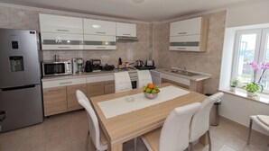 Una cocina moderna con una mesa de comedor, sillas blancas, un refrigerador de acero inoxidable, un microondas y un lavamanos.