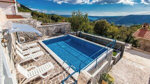Una piscina en la azotea con sillones de descanso, una terraza de piedra y una vista panorámica a las montañas.