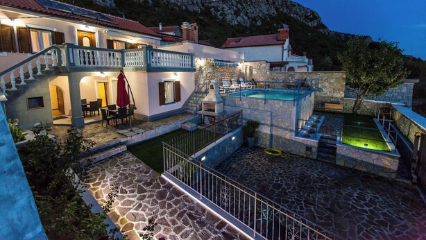 Una villa con piscina, mobiliario exterior y una escalera que lleva a un balcón.