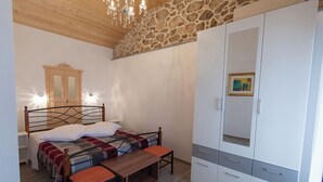 Un dormitorio con cama, mesita de noche, banco, armario y pared de piedra.