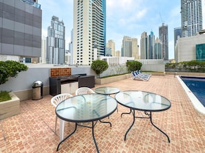A rooftop patio with glass tables and chairs, a barbecue grill, and a swimming pool. - Free Housekeeping Visits During Your Stay - Stayshort - Chic 1BR in Dubai Marina Sleeps 2 (Dubai)