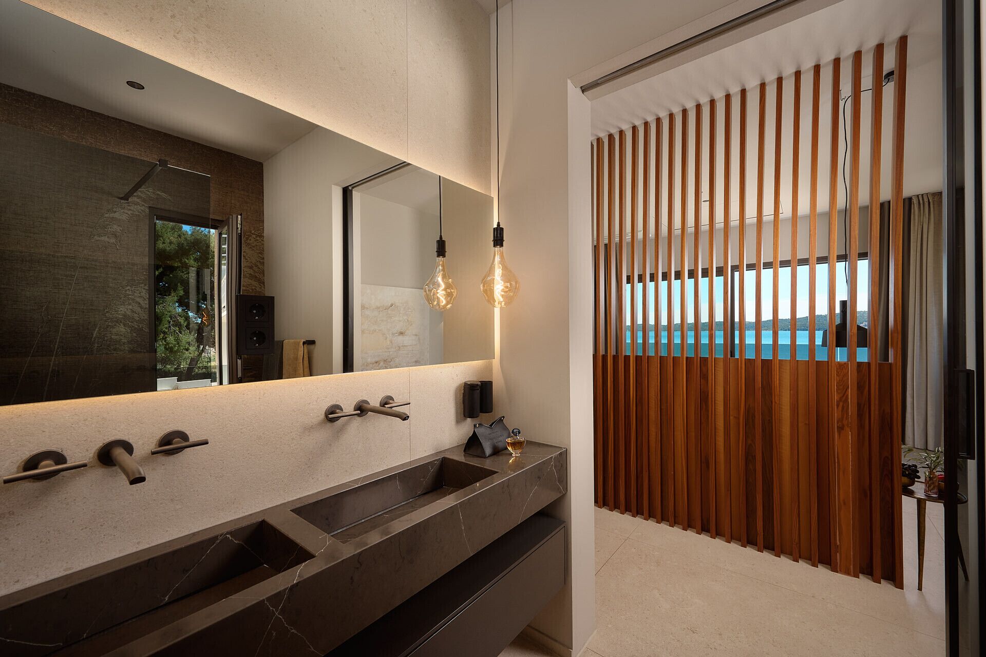 A modern bathroom with a large mirror, two sinks, and a wooden partition.