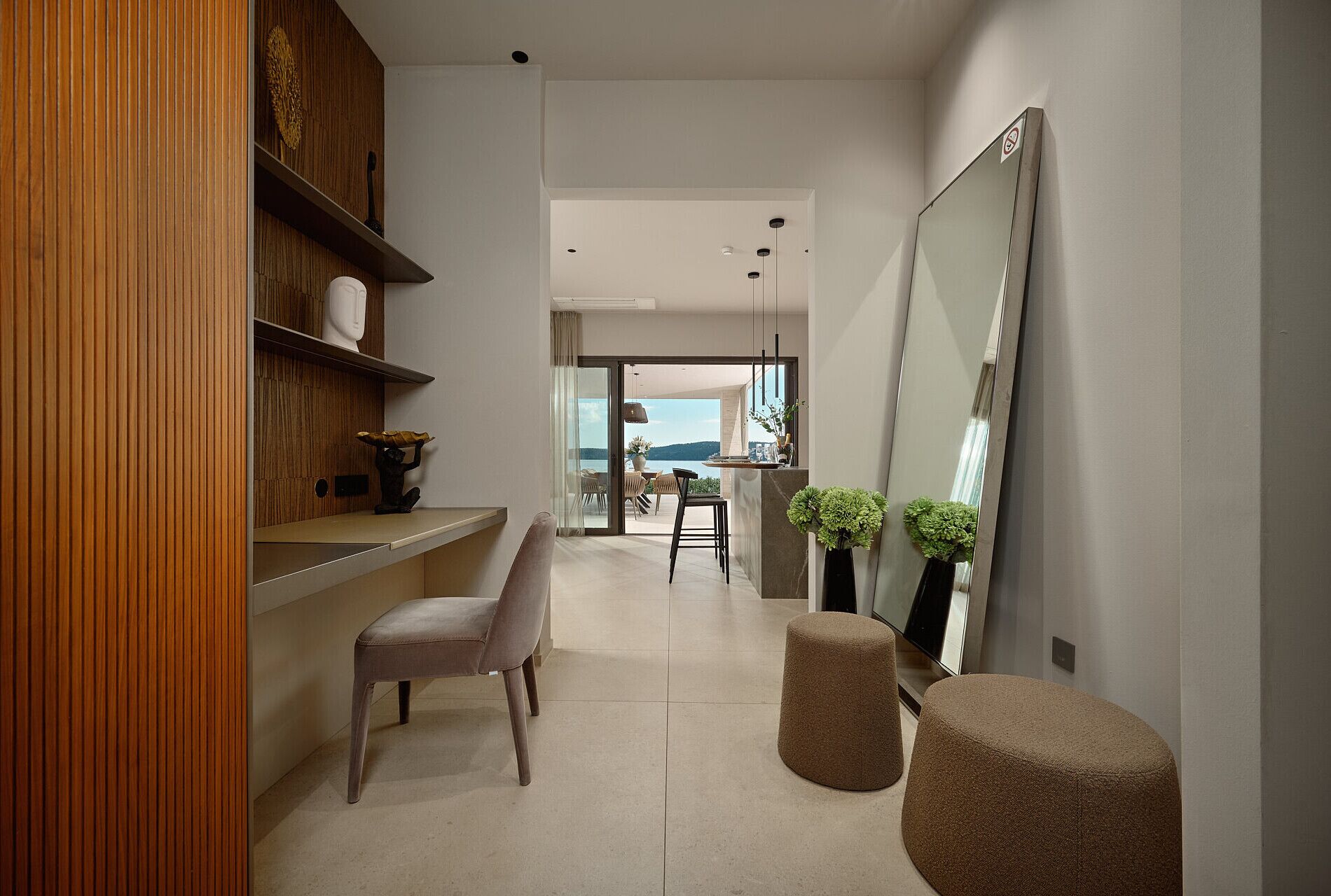 A modern interior with a wooden panel wall, a seating area with a chair and ottoman, a large mirror, and a view to an outdoor balcony.