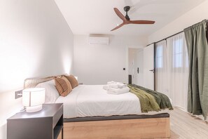 A bedroom with a bed, bedside table, ceiling fan, air conditioning unit, and a view of the outside through a window with curtains. - Suite Plaza Nueva. Comfort in the center of Granada (Granada)