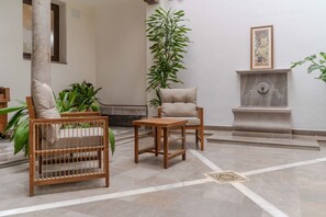 A lobby with a wooden bench, a small table, a tall plant, a chair, and a fireplace. - Suite Plaza Nueva. Comfort in the center of Granada (Granada)