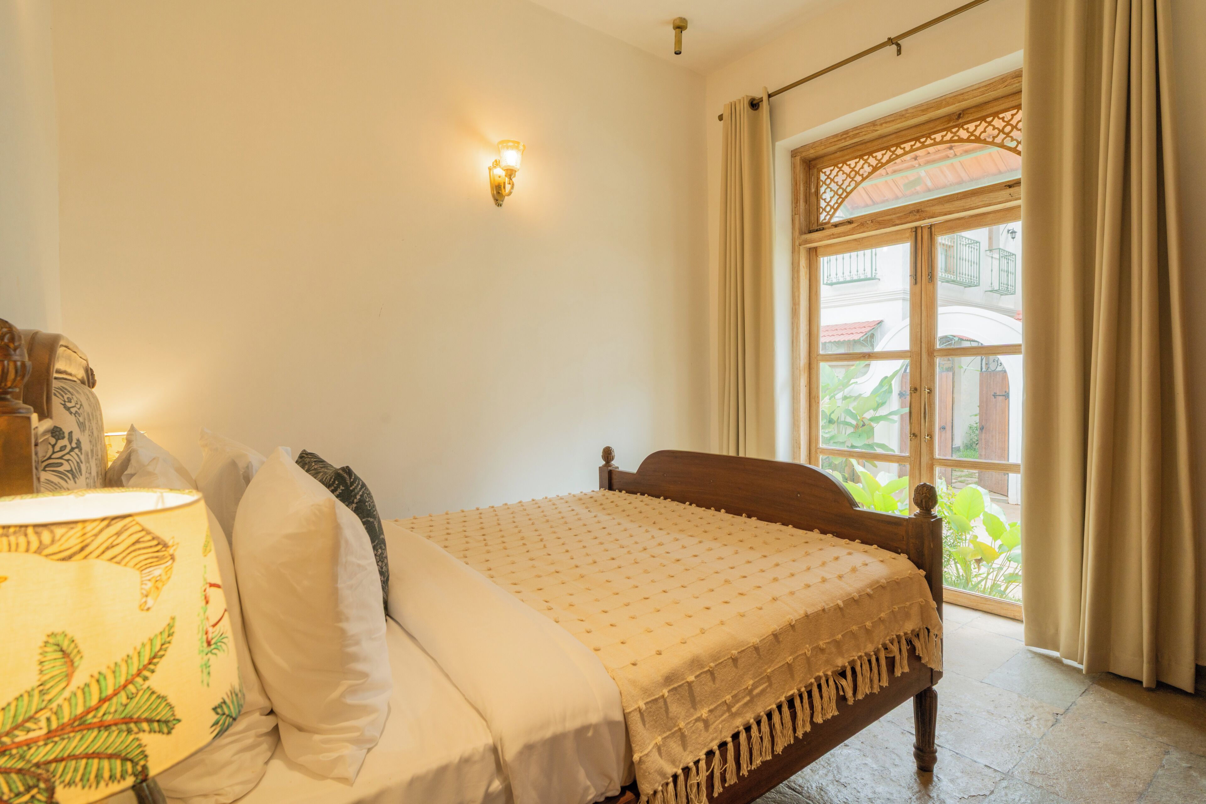 A bedroom with a bed, a lamp, a wall-mounted light, and a window with curtains.
