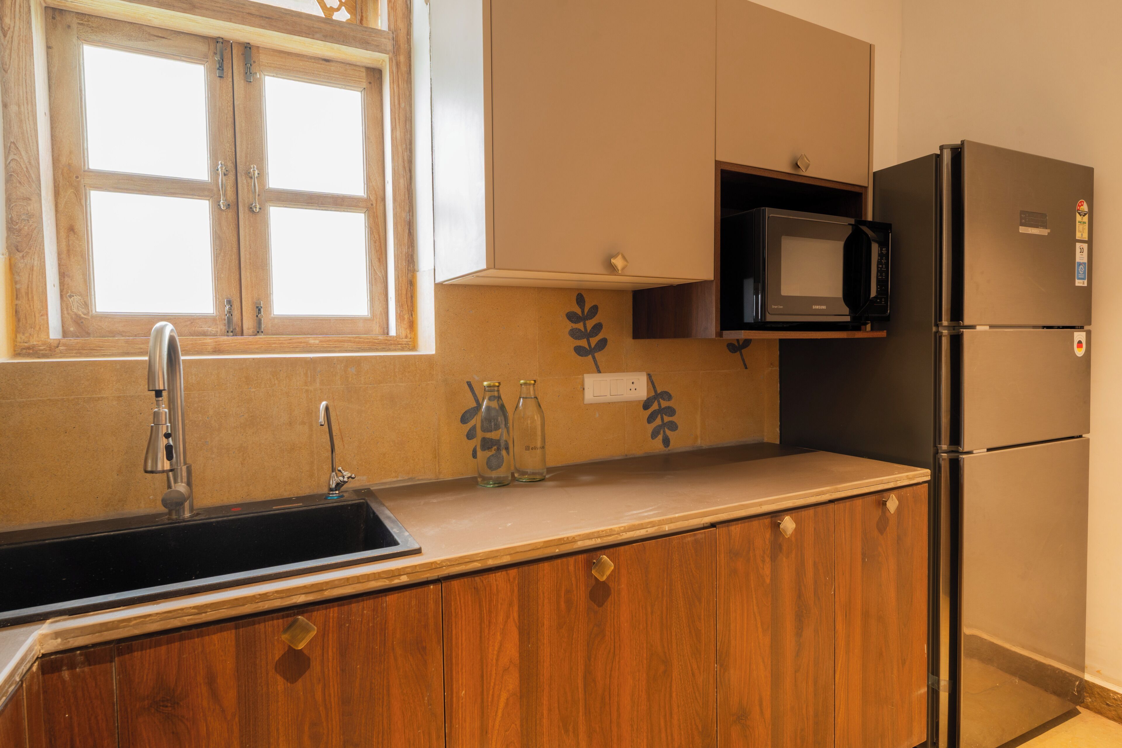 Una cocina con armarios de madera, un lavamanos de acero inoxidable, un microondas y un refrigerador.