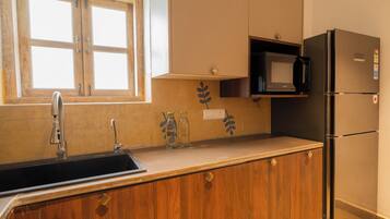 Una cocina con armarios de madera, un lavamanos de acero inoxidable, un microondas y un refrigerador.