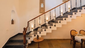Una escalera con barandilla de madera y balaustradas negras, una mesa redonda con un objeto decorativo, y una mesa de comedor lista con platos y cubiertos.