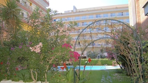 Ein Hotelinnenhof mit Schwimmbecken, einem Garten mit unterschiedlichen Pflanzen und einem mehrstöckigen Gebäude im Hintergrund.