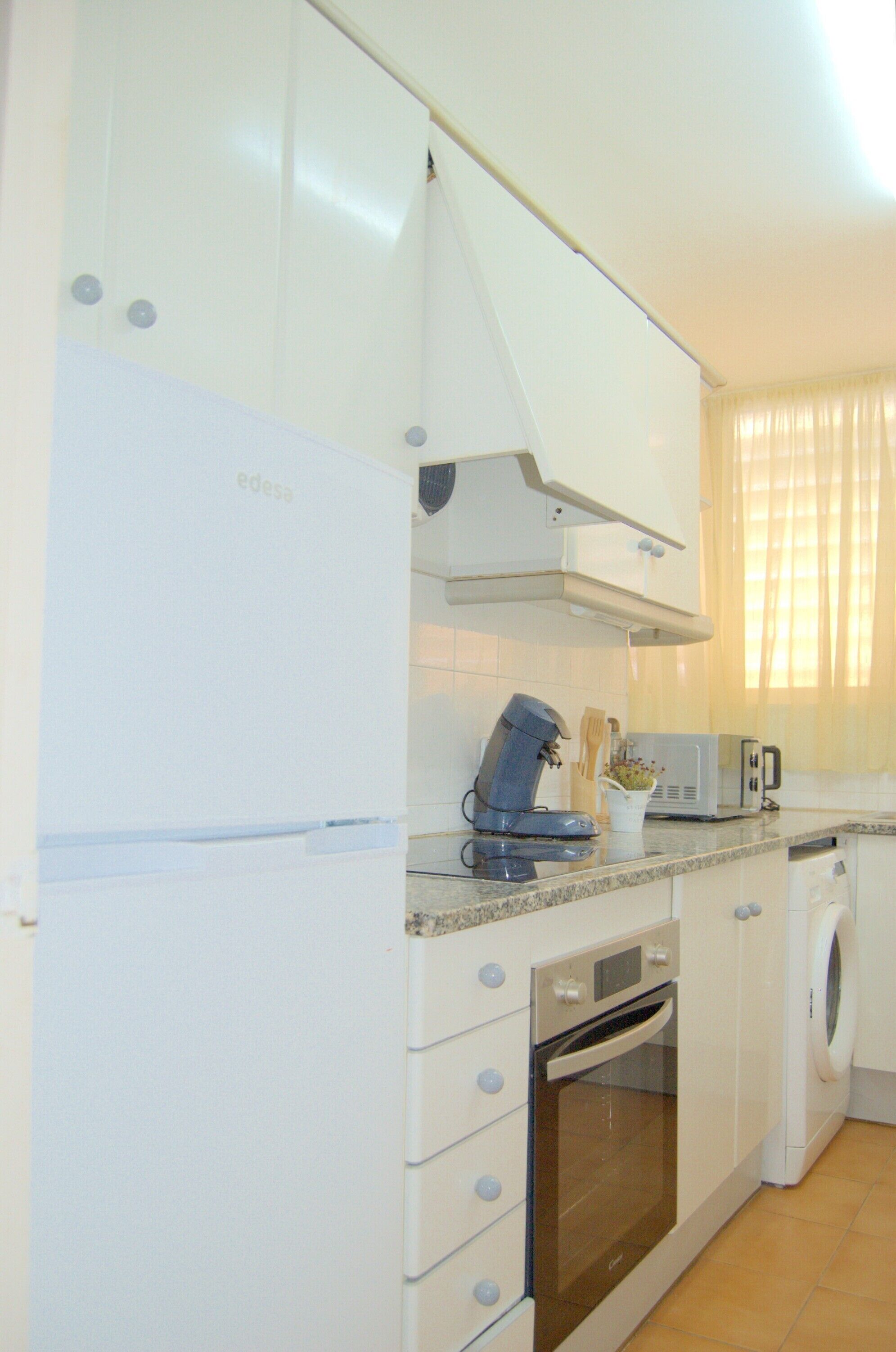 Uma cozinha compacta com forno embutido, micro-ondas e máquina de lavar.