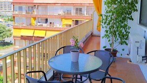 Ein Balkon mit rundem Tisch und Stühlen, einem Blumentopf, einer Klimaanlage und Blick auf Gebäude im Hintergrund.