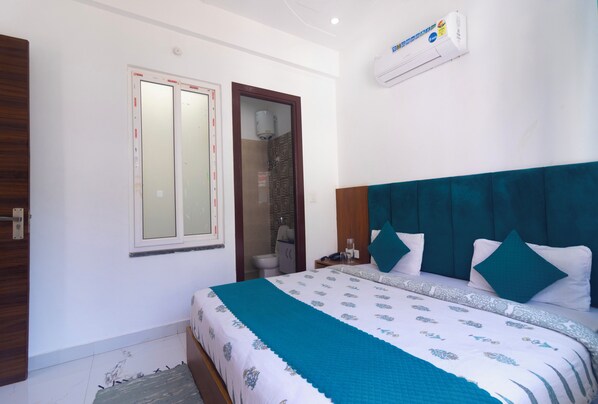 A bedroom with a bed, a window, a door, and an air conditioning unit. - Hotel Parth Inn (Rishikesh)
